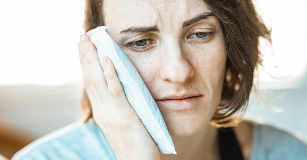 woman holding icepack to side of face where wisdom tooth is causing pain