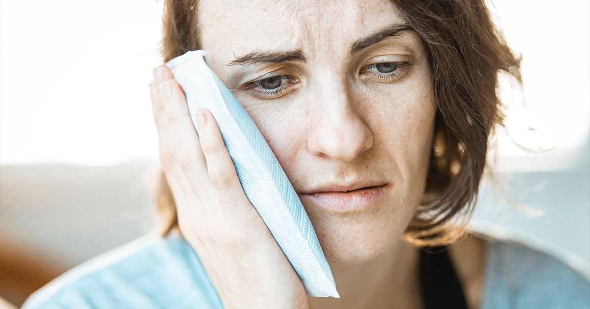 woman holding icepack to side of face where wisdom tooth is causing pain