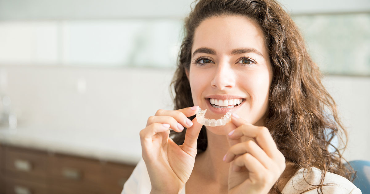 Dental invisible braces or silicone trainer in the hands of a young smiling girl. Orthodontic concept - Clear braces.